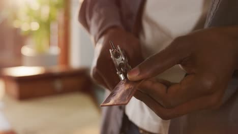 hands of african american craftsman using tools to make a hole in leather workshop