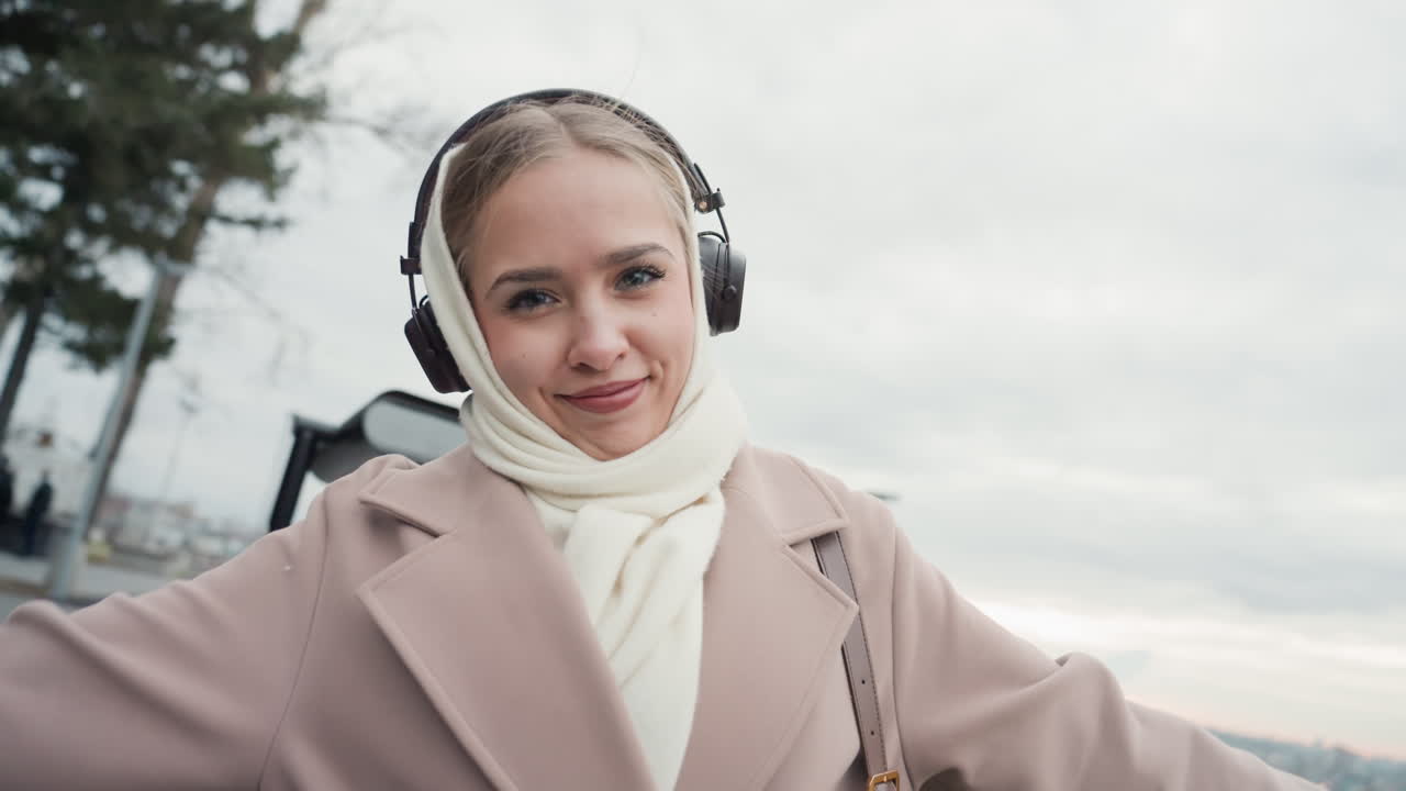 Smiling lady with city view. Caucasian female leaning on rail smiling at skyline with scarf and coat. Cityscape scene featuring woman in overcoat and scarf observing urban park reflection