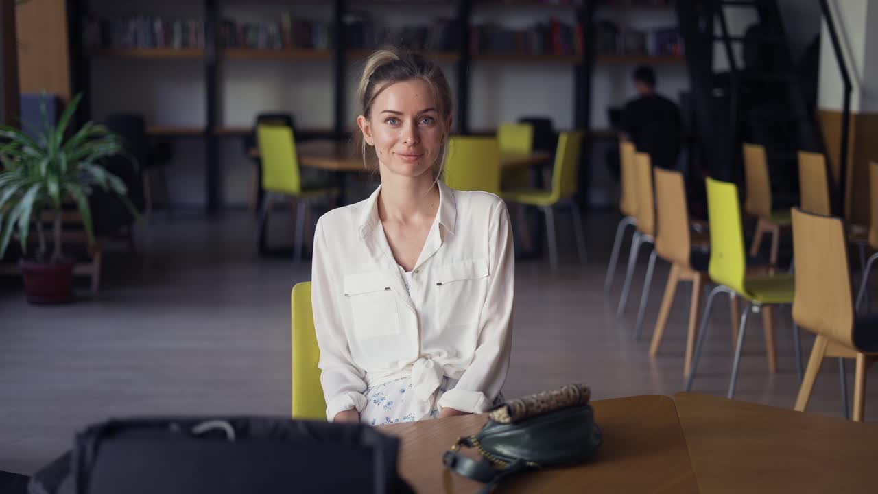 Ritratto di una giovane donna sorridente che guarda la telecamera, con uno scaffale di libri sullo sfondo.