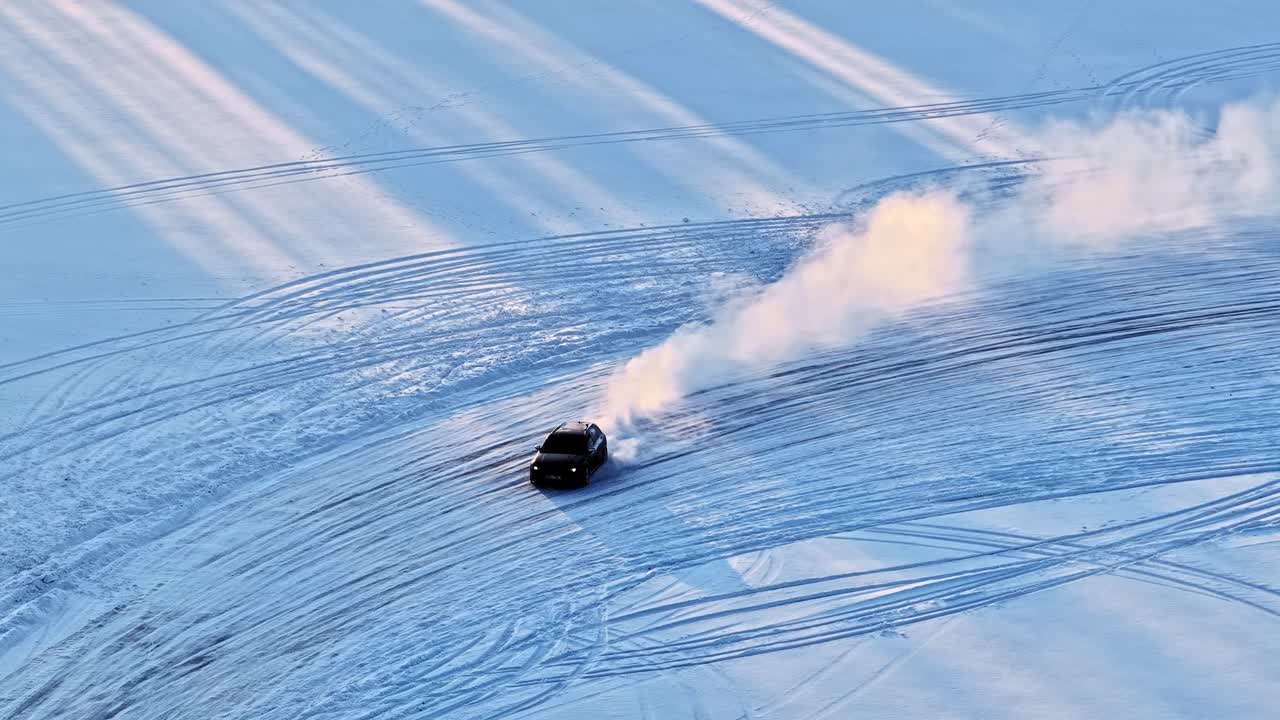 Se et luftfoto af en bil, der dygtigt drifter hen over sneen og efterlader spor i et vinterlandskab.