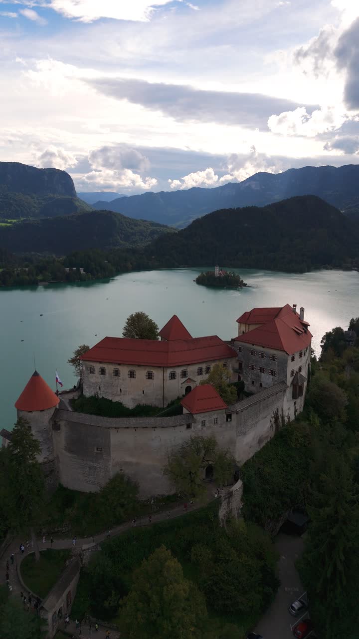 Verticale, aerea: il castello di Bled si affaccia sul lago di Bled di giorno, con foreste e paesaggi a Bled, Slovenia, ripresa drone in avvicinamento