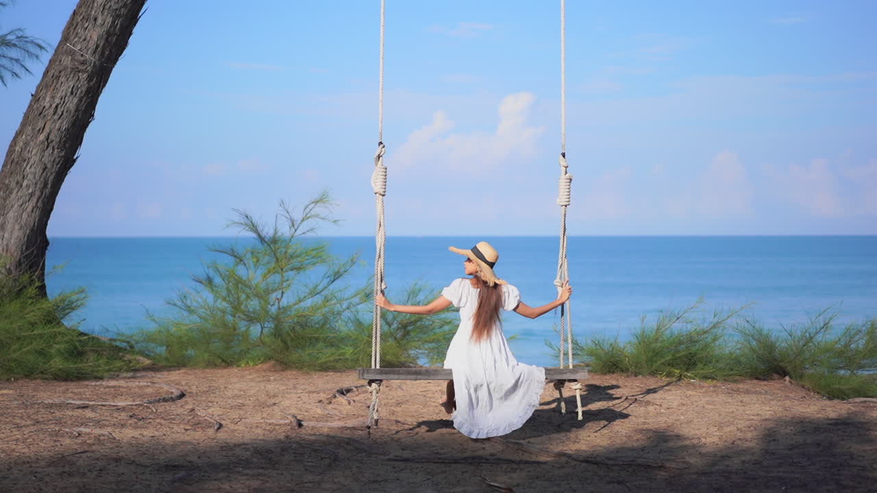 Una giovane donna con un abito svolazzante si gode un'altalena con vista sull'oceano.
