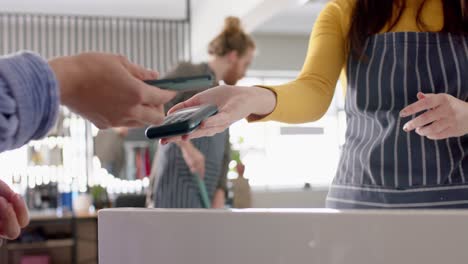sección media de una peluquera caucásica y un cliente pagando con un teléfono inteligente, en cámara lenta
