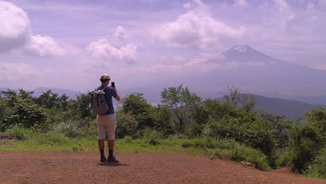 Male-hiker-taking-pictures-with-his-smartphone-from-top-of-Mountain-looking-towards-Mount-Fuji