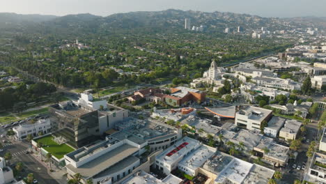 Drone-Volando-Sobre-Beverly-Hills,-Montaña-Verde-En-El-Horizonte-Con-Tejados-Y-Calles-Concurridas-Debajo