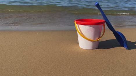 children empty bucket with blue scoop on sandy beach with waves breaking on sea shore