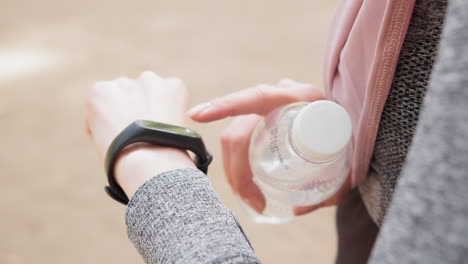 Woman using smartwatch and holding water bottle during outdoor activity