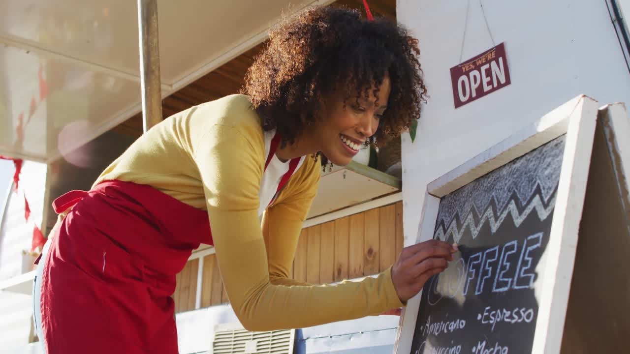 Donna afroamericana con grembiule che scrive sul menù lavagna del food truck