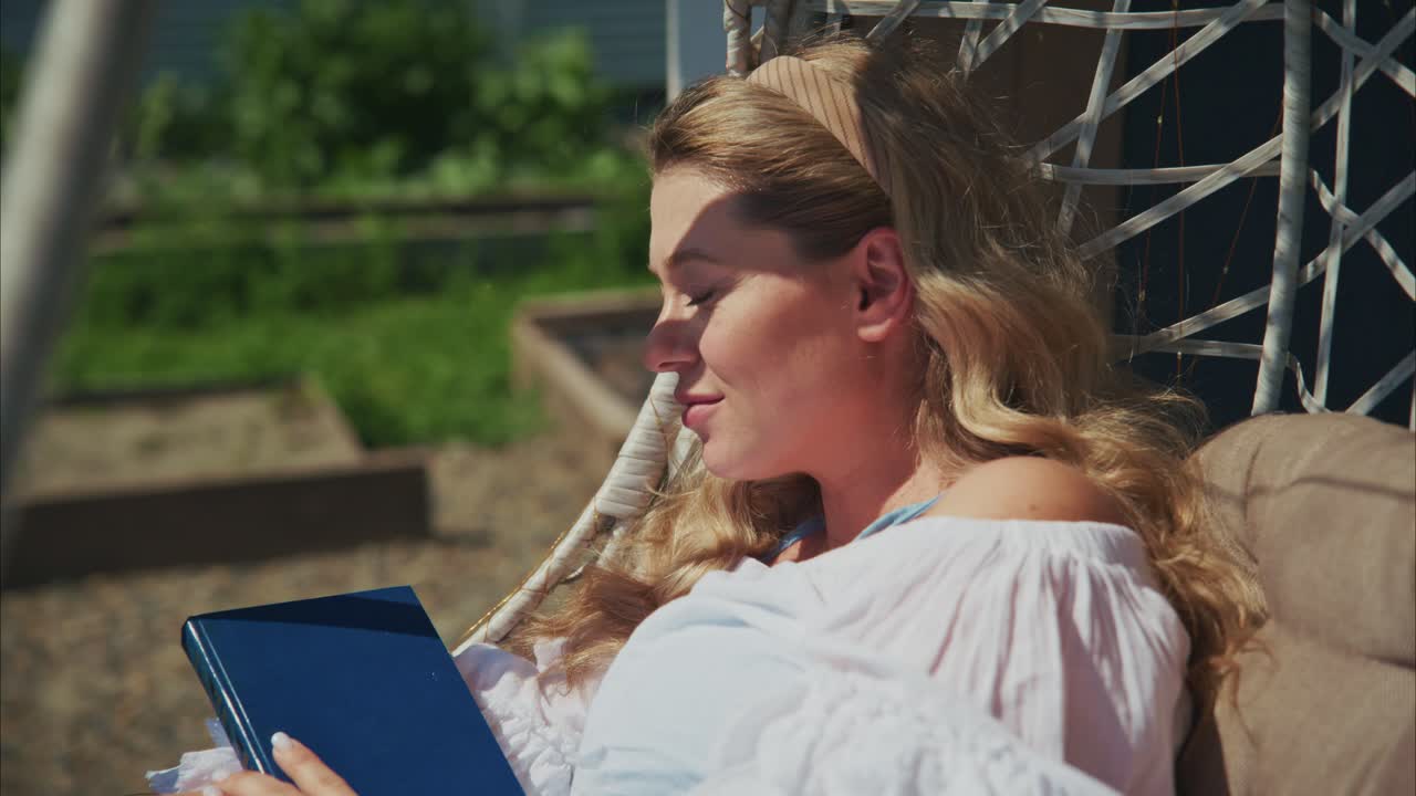 Happy Woman Relaxing and Reading a Book in a Garden Swing Chair