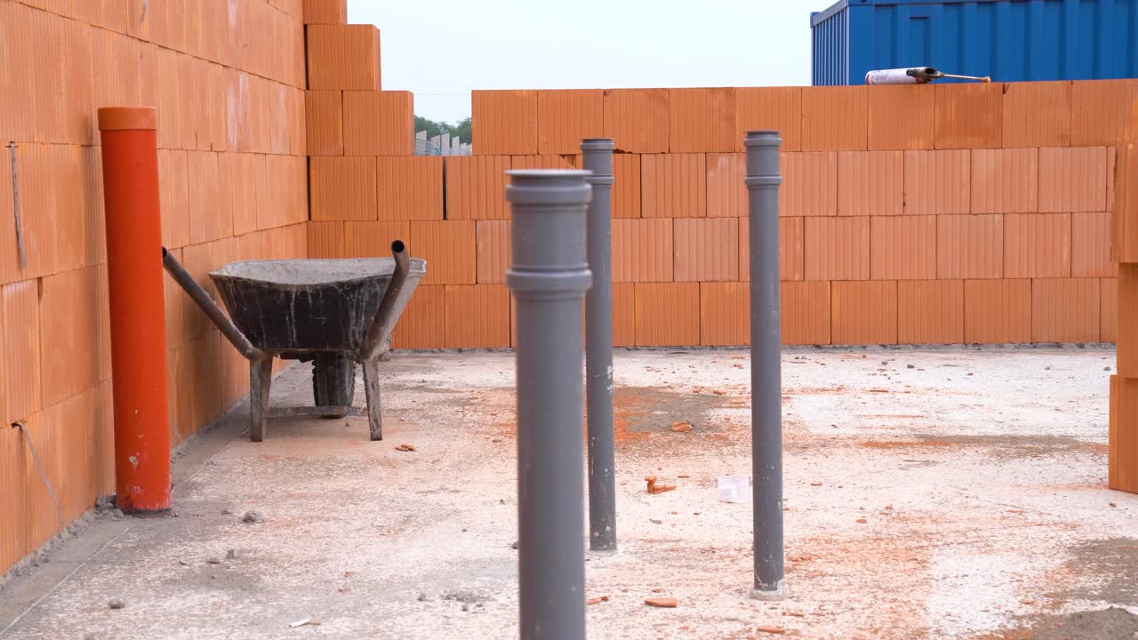Exposed pipes and wheelbarrow on concrete floor of house under construction