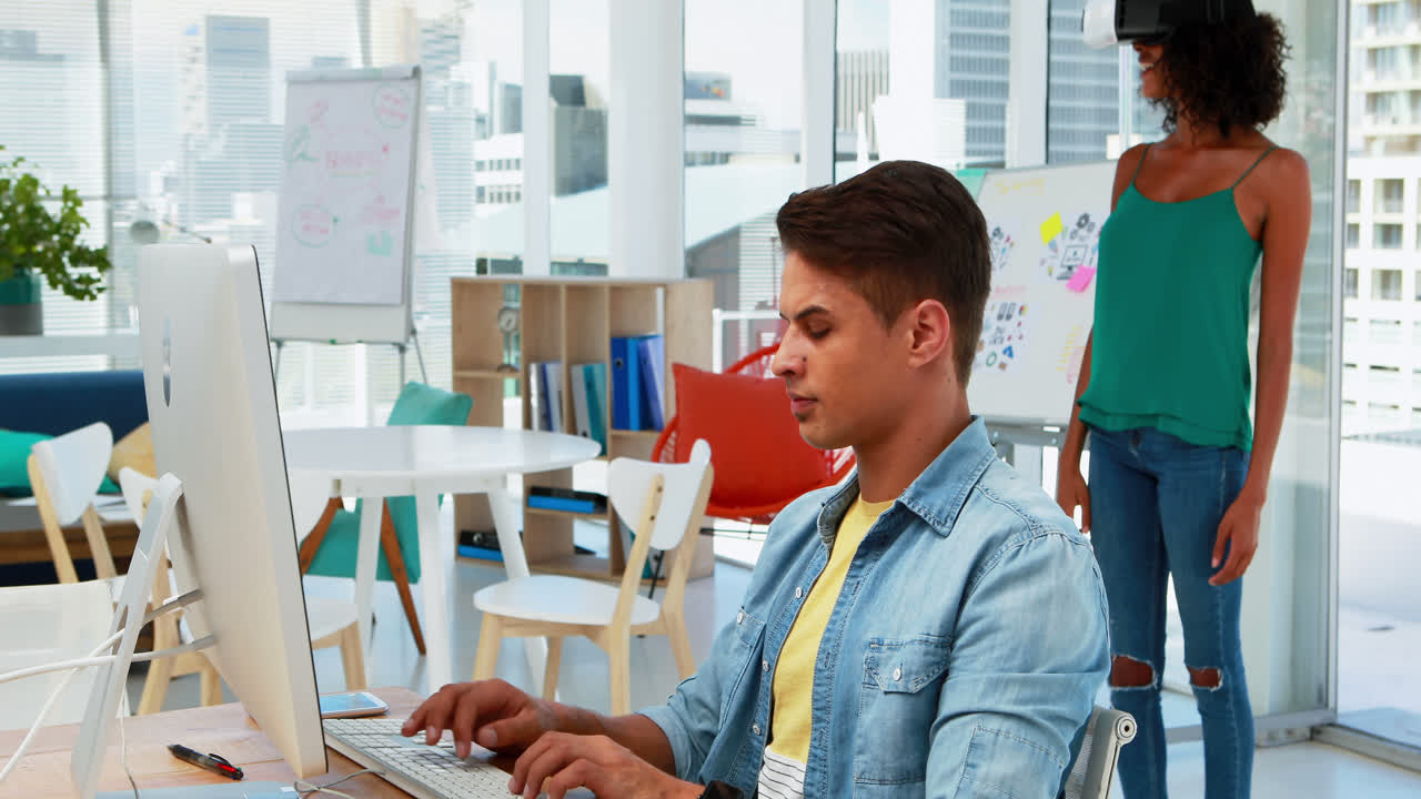 ejecutivo masculino trabajando en la computadora mientras que el ejecutivo femenino usando auriculares de realidad virtual 4k