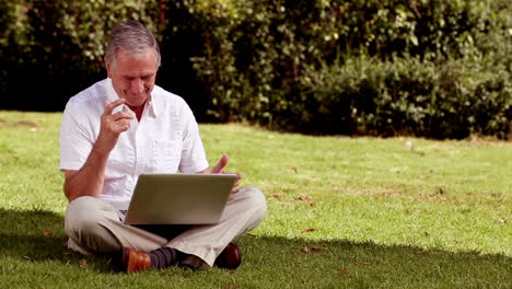 Mature-man-sat-on-the-grass-using-his-laptop