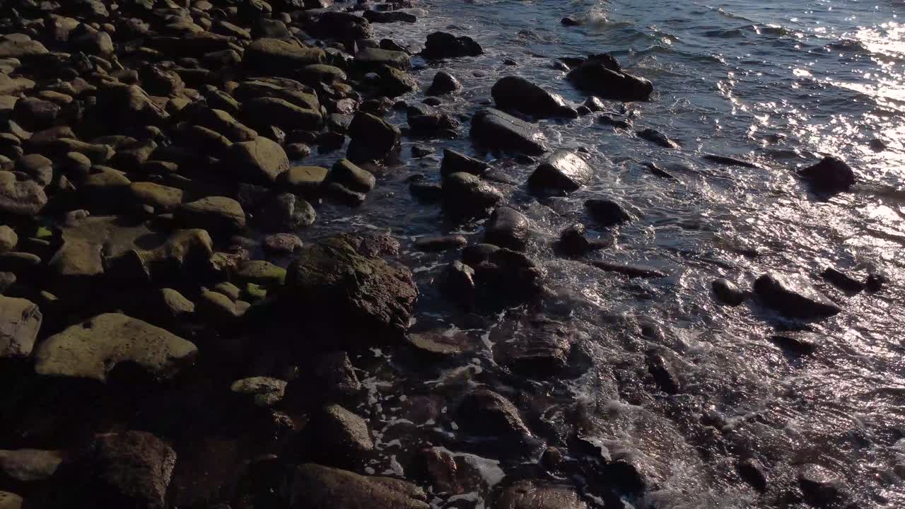 Ripresa aerea con drone a bassa quota di onde turchesi che si infrangono su una spiaggia rocciosa