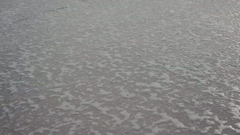 Close-up-of-sea-water-surface-with-intricate-patterns-of-foam-at-Ovar-Beach,-Portugal