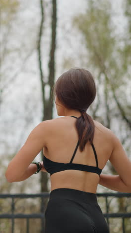 Young athlete training outdoors near iron fence with trees in background, practicing fitness routine and stretching for strength and flexibility in natural surroundings