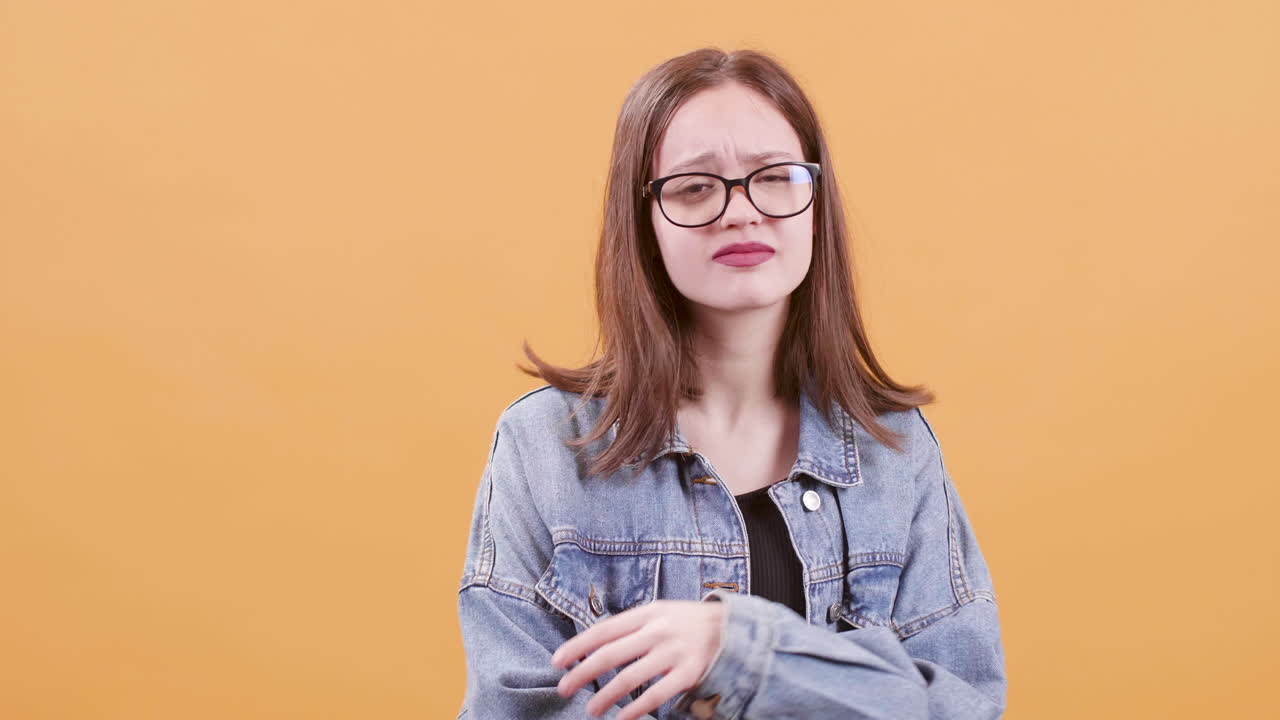 A woman with eyeglasses and a denim jacket expressing doubt and confusion