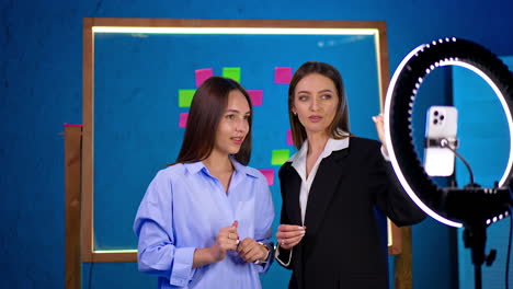 women recording a video together indoors. two women are engaging in a video recording session using a ring light for better lighting in a creative room