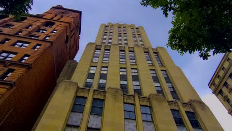 bottom-to-top-angle-view-looking-up-blue-skies-some-white-clouds-passing-by-on-a-sunny-summer-day-at-iconic-version-of-the-daily-planet-from-the-comic-book-style-building-as-birds-bikes-and-cars-go