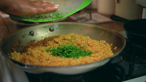 adding chopped basil and bacon to a sizzling skillet of couscous on the stove in slow motion