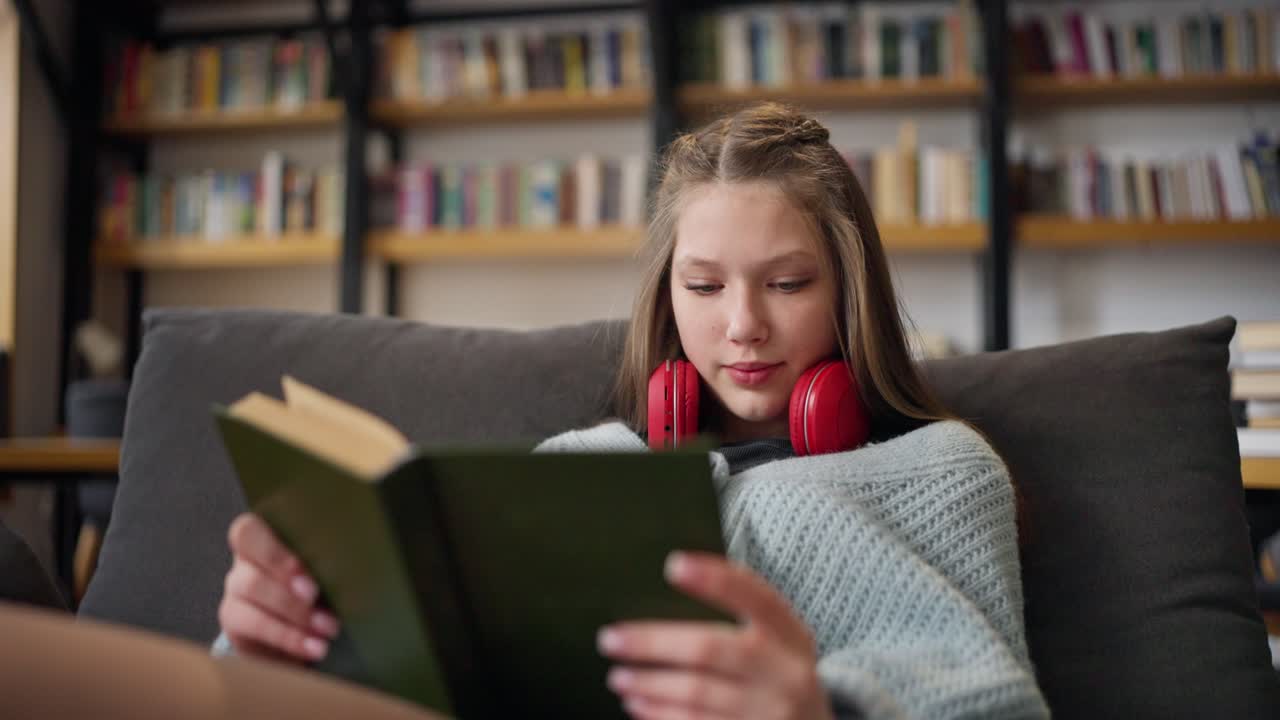 Teenage girl reading a book on a couch in a library