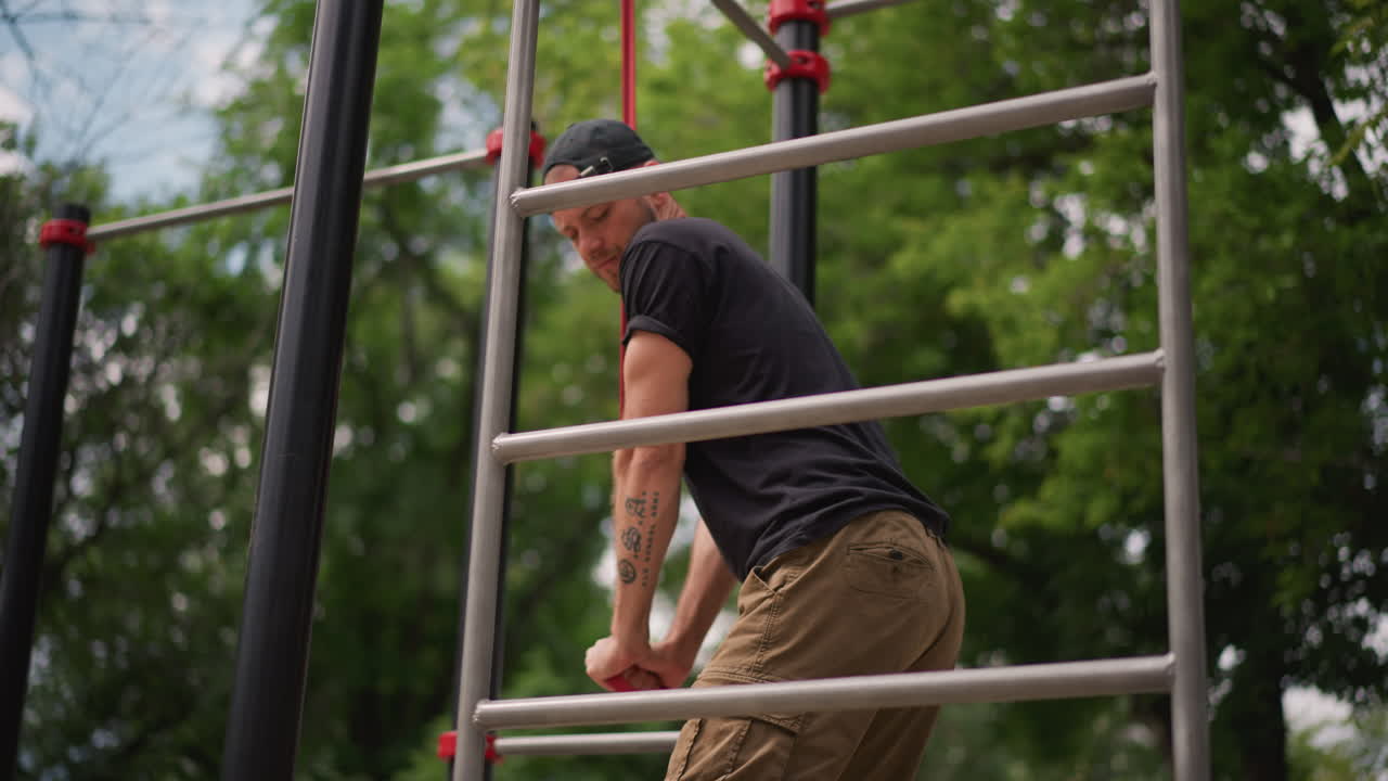 Man Ascends Bars, Person Skillfully Pulls Up On Metal Bars Amid Leafy Canopy Environment, Man Climbs Metal Structure With Focused Grip Technique Surrounded By Lush Natural Foliage And Trees