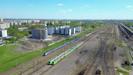 disparo aéreo escénico de un tren de pasajeros que conduce hacia el atardecer en vías de tren rodeadas de árboles por encima del paisaje urbano hacia adelante
