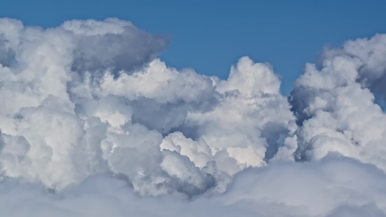 Towering cumulus clouds rising into clear blue sky in daytime aerial view from atmosphere