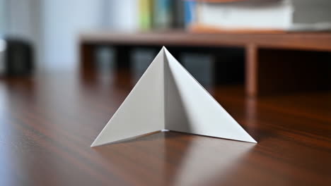 a white paper object, possibly an origami bookmark or a folded paper airplane, resting on a polished wooden desk