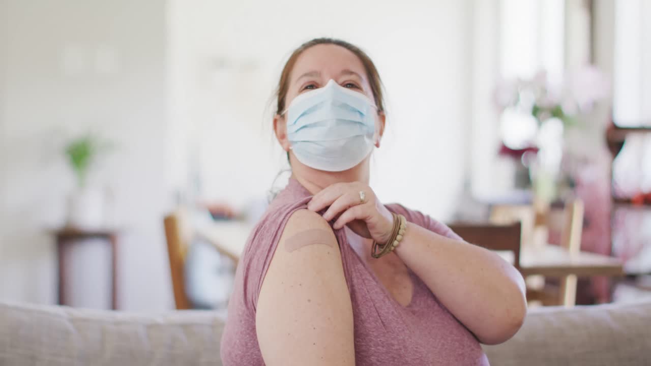 Caucasian woman wearing face mask pointing at bandage on her arm