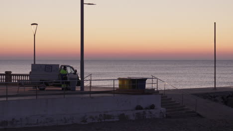 garbage collector works peacefully next to a truck on a beach early in the morning