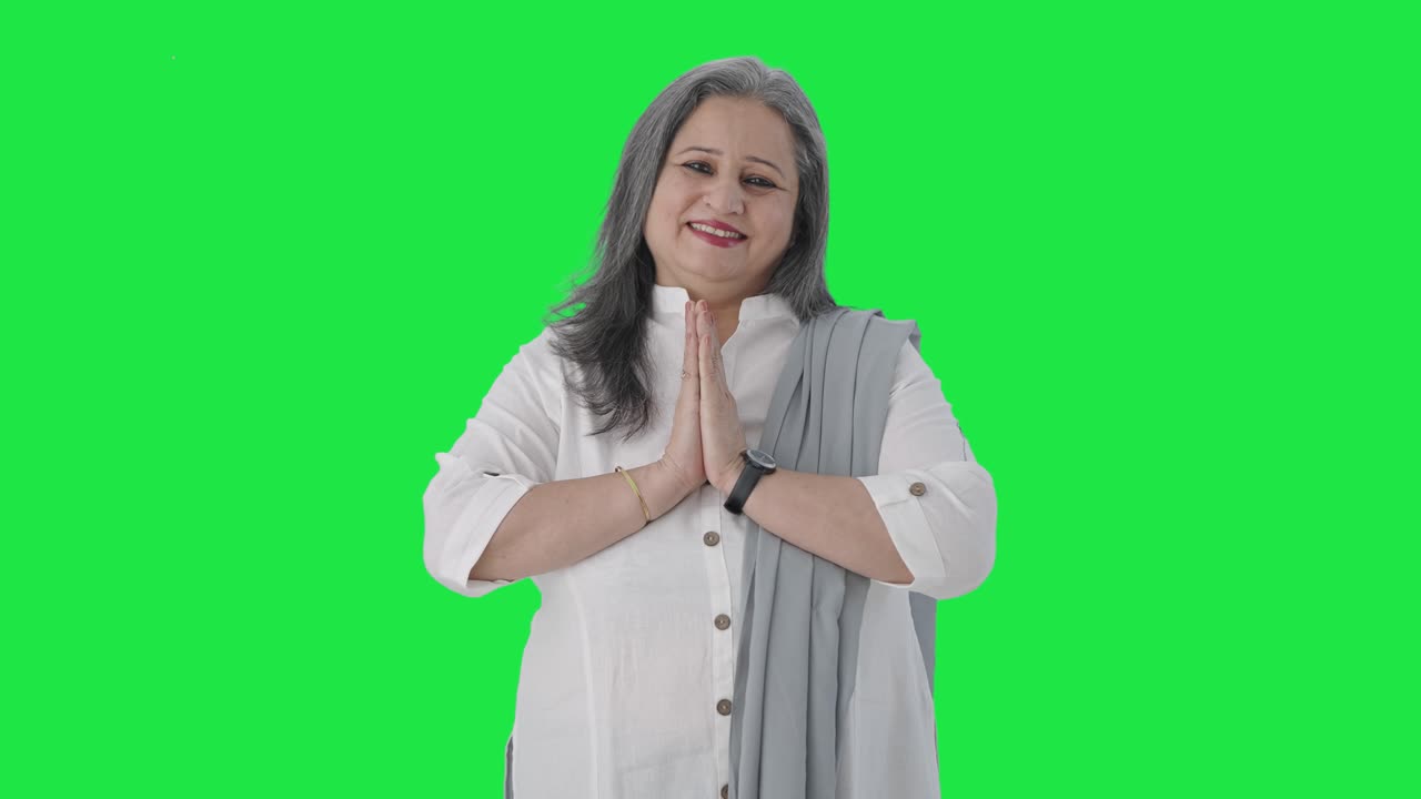 Happy Indian senior businesswoman greeting and doing Namaste Green screen