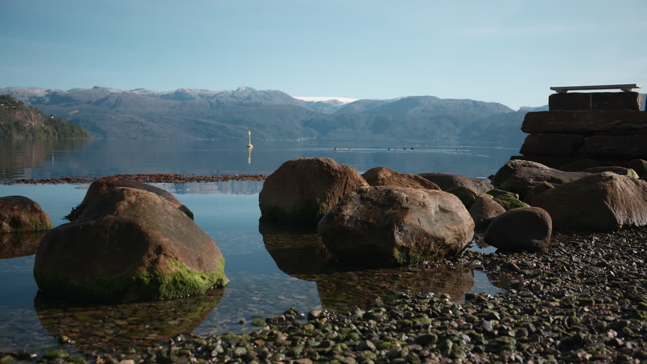 The water flows slowly into the beach on a sunny day in Hardangerfjord, Norway