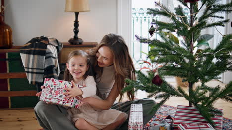 mujer curiosa niño sacudiendo regalo en la casa de año nuevo. celebración familiar amorosa