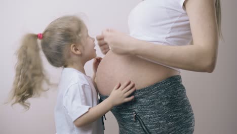 girl hides head under pregnant mommy t-shirt at white wall