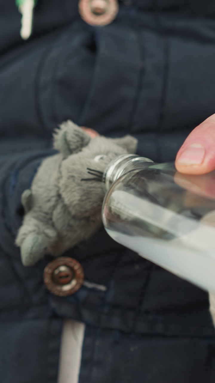 el hombre le da bebida de una botella de vidrio al ratón. el animal se asoma de la ropa masculina. el mago revive al ratón de juguete con una poción mágica para bromear de cerca