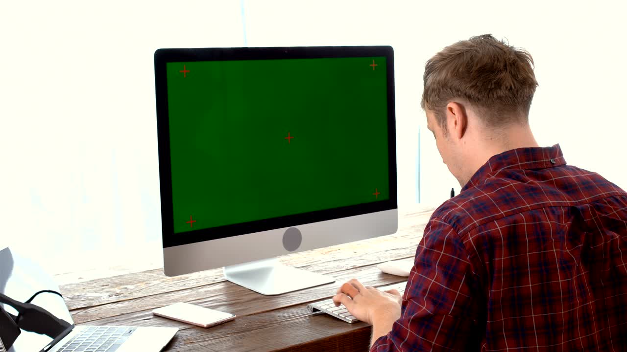 joven usando una computadora con un monitor de pantalla verde trabajando en casa