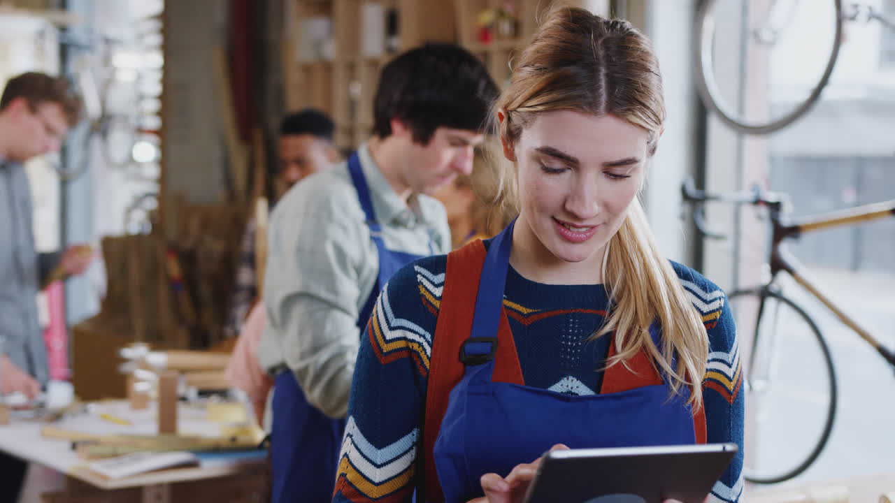 Handwerkerin in einer Holzwerkstatt, die Fahrradrahmen baut und ein digitales Tablet verwendet.