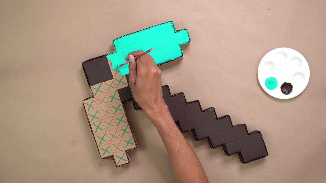 Overhead view of hands painting pixel-style pickaxe made from cardboard for a DIY project