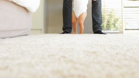 father helping baby to walk across rug