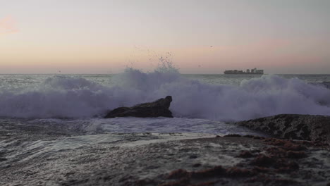 Las-Olas-Chocan-Contra-Las-Rocas-Con-Un-Buque-De-Carga-En-El-Fondo