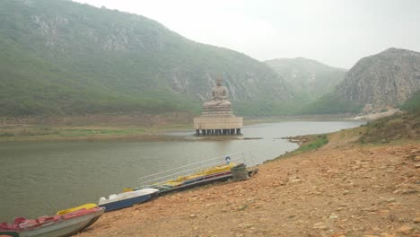 estatua de buda de 70 pies de altura en el lago ghora katora rodeada de montañas bajo un cielo brumoso, rajgir