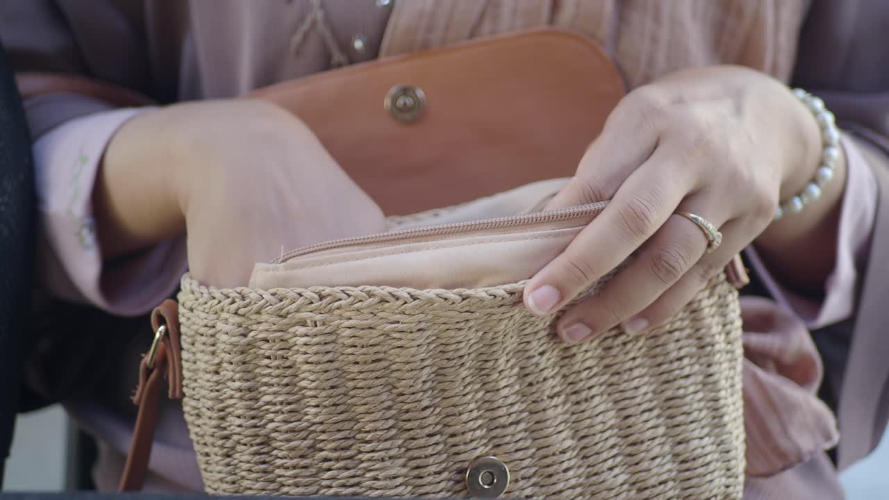 Mani di donna che si protendono in una borsa di paglia intrecciata