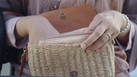 woman's hands reaching into a woven straw handbag