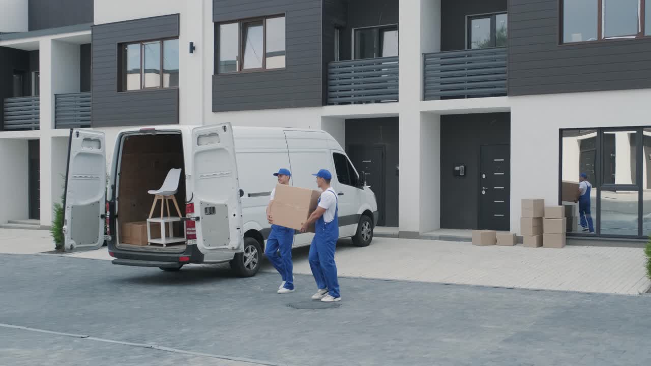 Two young workers of removal company are loading boxes and furniture into a minibus