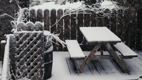 snow falling on fence, bench and table