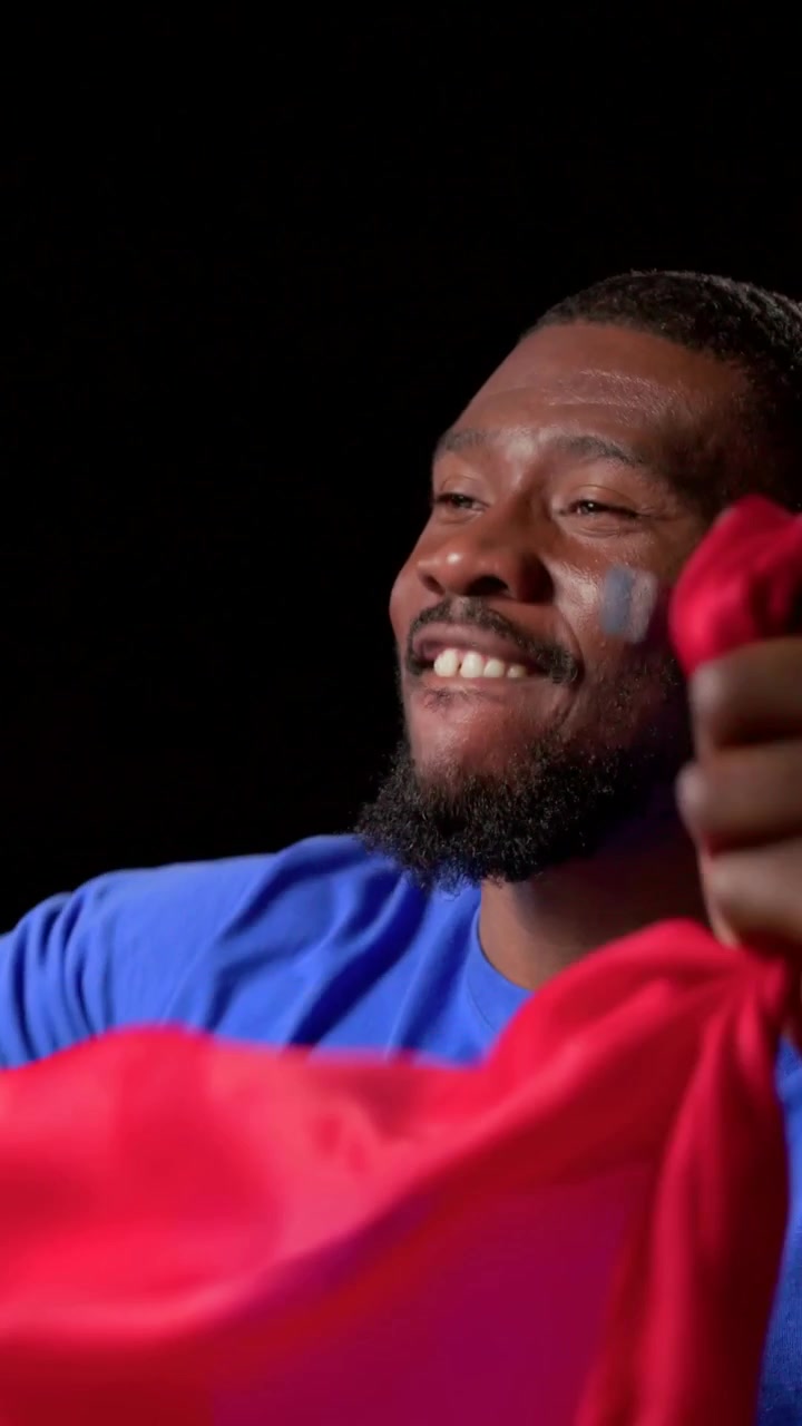 Video vertical: Hombre entrando por la izquierda con camiseta azul y pintura facial, ondeando una bandera, con tela roja de animación y espacio para texto.
