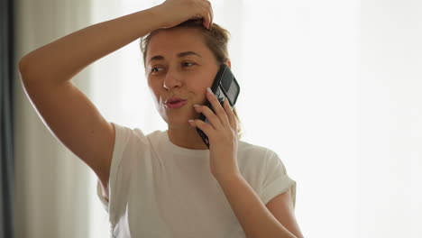 lady uses phone jogging at residence closeup. positive woman communicates via smartphone while touching hair on treadmill. runner training with cellphone