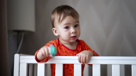 lovely baby boy in the crib stretches hand with a pacifier. cute child looks around and banging his hand at the cot. close up.