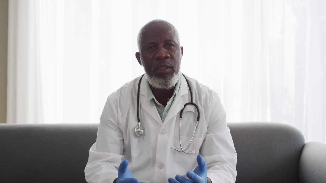 Portrait of male african american doctor wearing surgical gloves talking while having a videocall