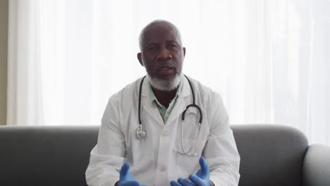 retrato de un médico afroamericano que usa guantes quirúrgicos hablando mientras tiene una videocall